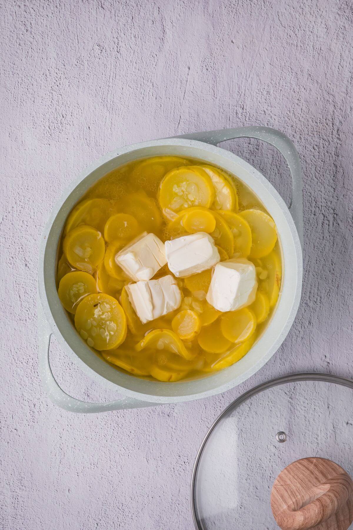 Squash, onion, broth, and avocado oil simmering in a pot with cream cheese melting in