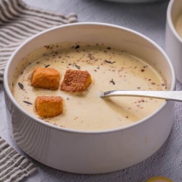 Yellow squash soup in a bowl with croutons.