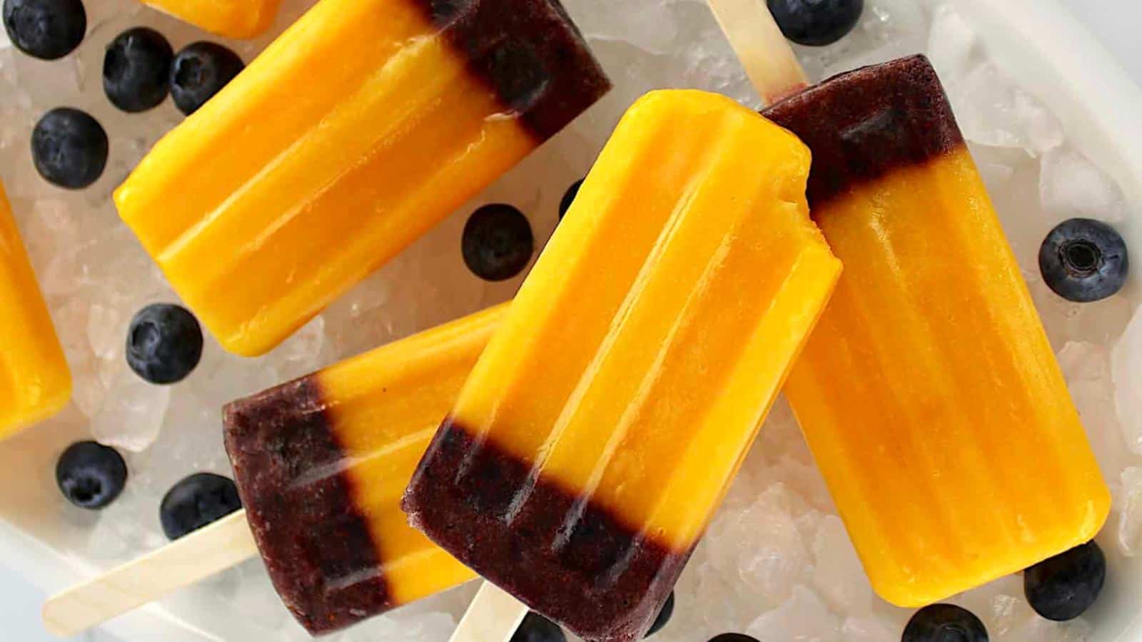 Mango and blueberry layered popsicles on ice, surrounded by fresh blueberries.
