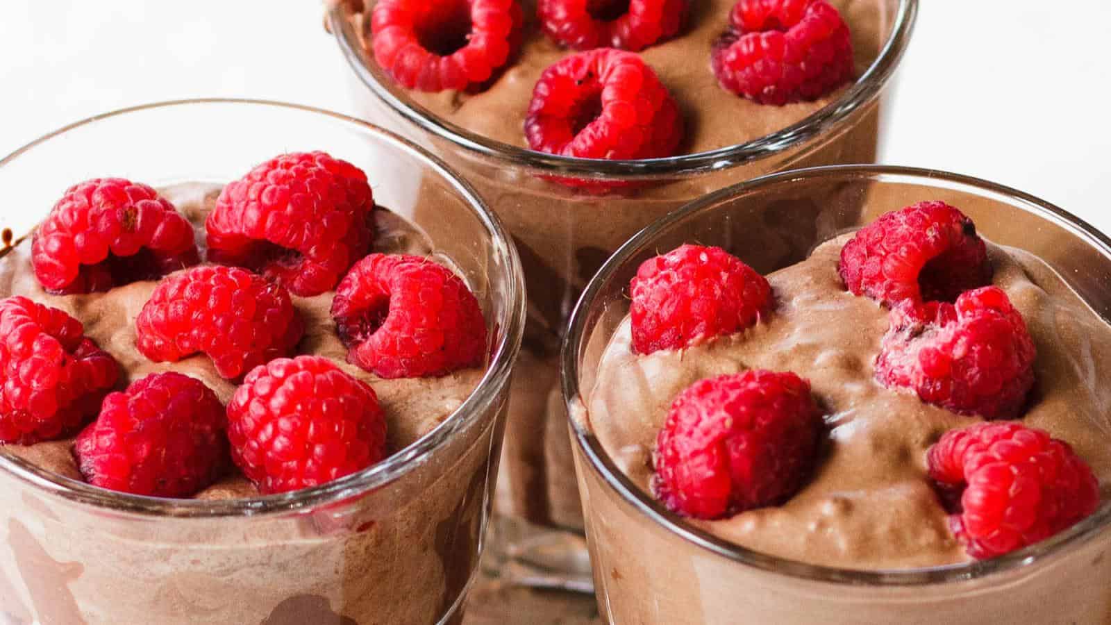Three glasses filled with chocolate mousse and topped with fresh raspberries.