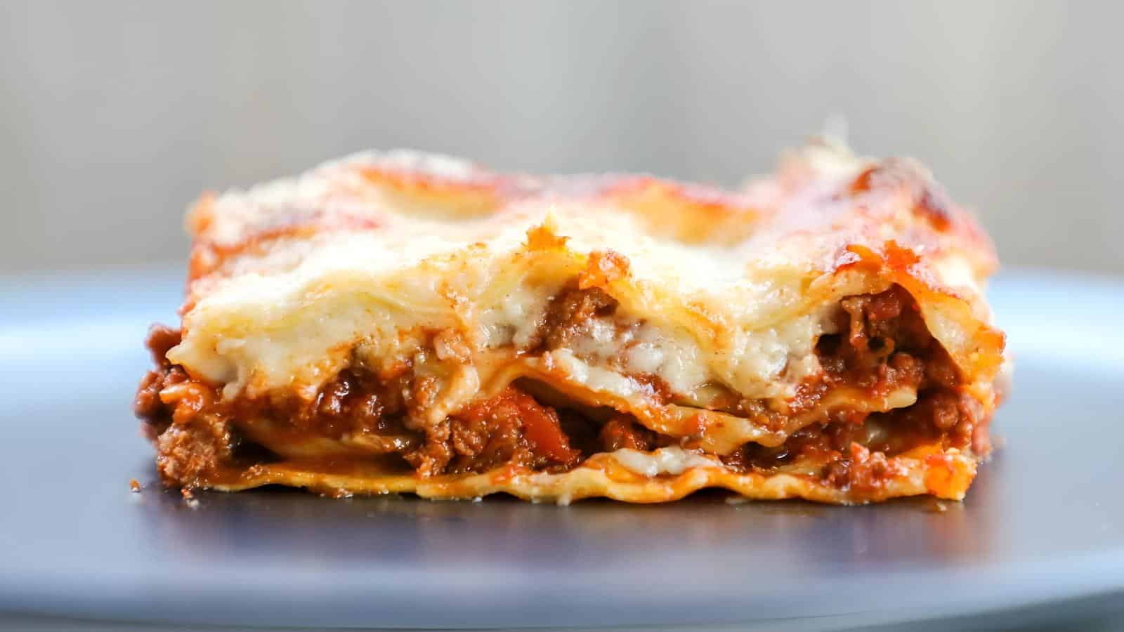 A close-up of a slice of lasagna showing layers of pasta, meat sauce, and melted cheese on a blue plate.