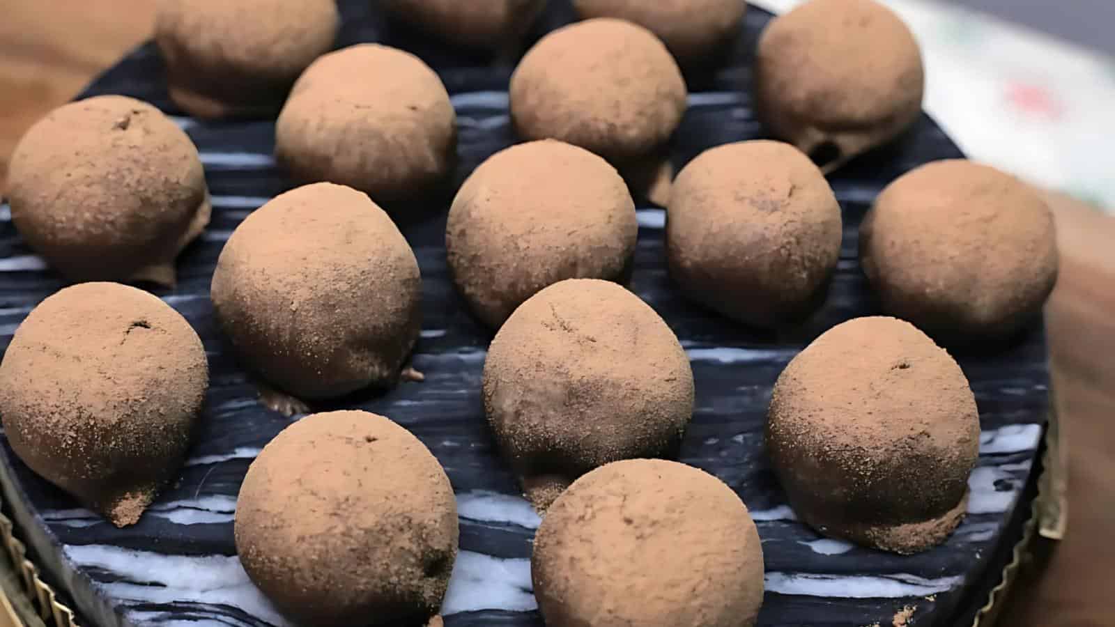 Rows of round chocolate truffles coated in cocoa powder are arranged on a black and white marble surface.
