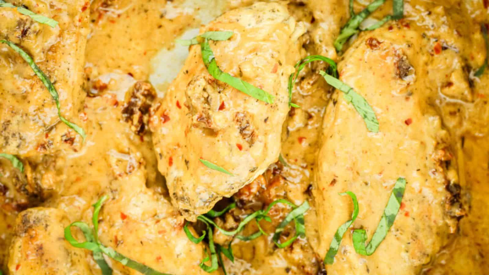 Chicken wings coated in a creamy sauce with herbs and spices, garnished with thin strips of fresh green basil leaves.