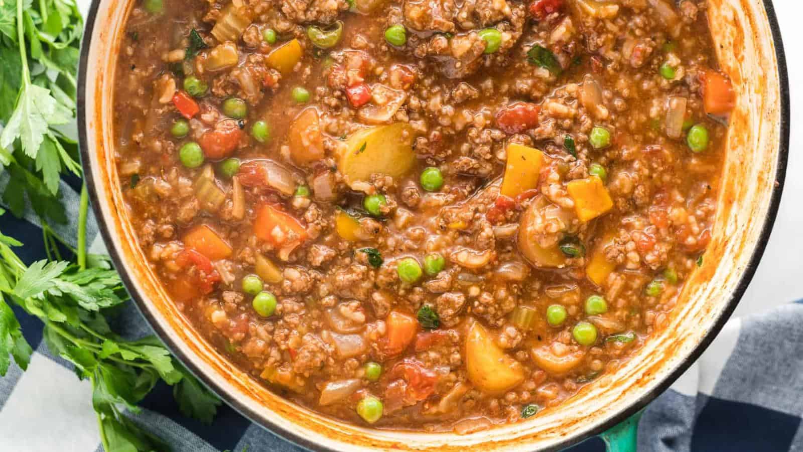 A pot filled with hearty beef stew containing ground beef, potatoes, carrots, peas, tomatoes, and herbs.