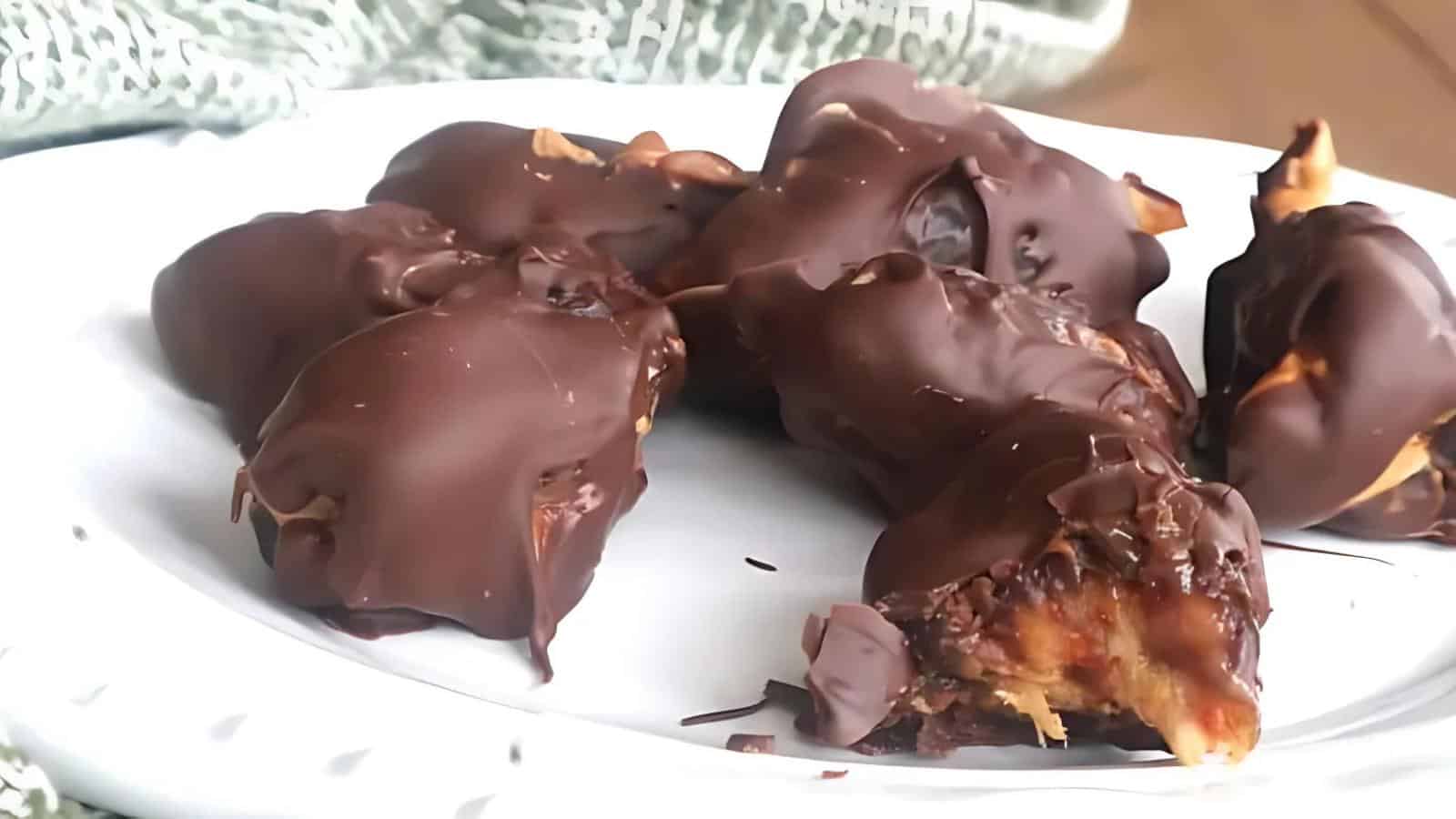Five chocolate-covered banana pieces with peanut butter filling on a white plate, one piece with a bite taken out.
