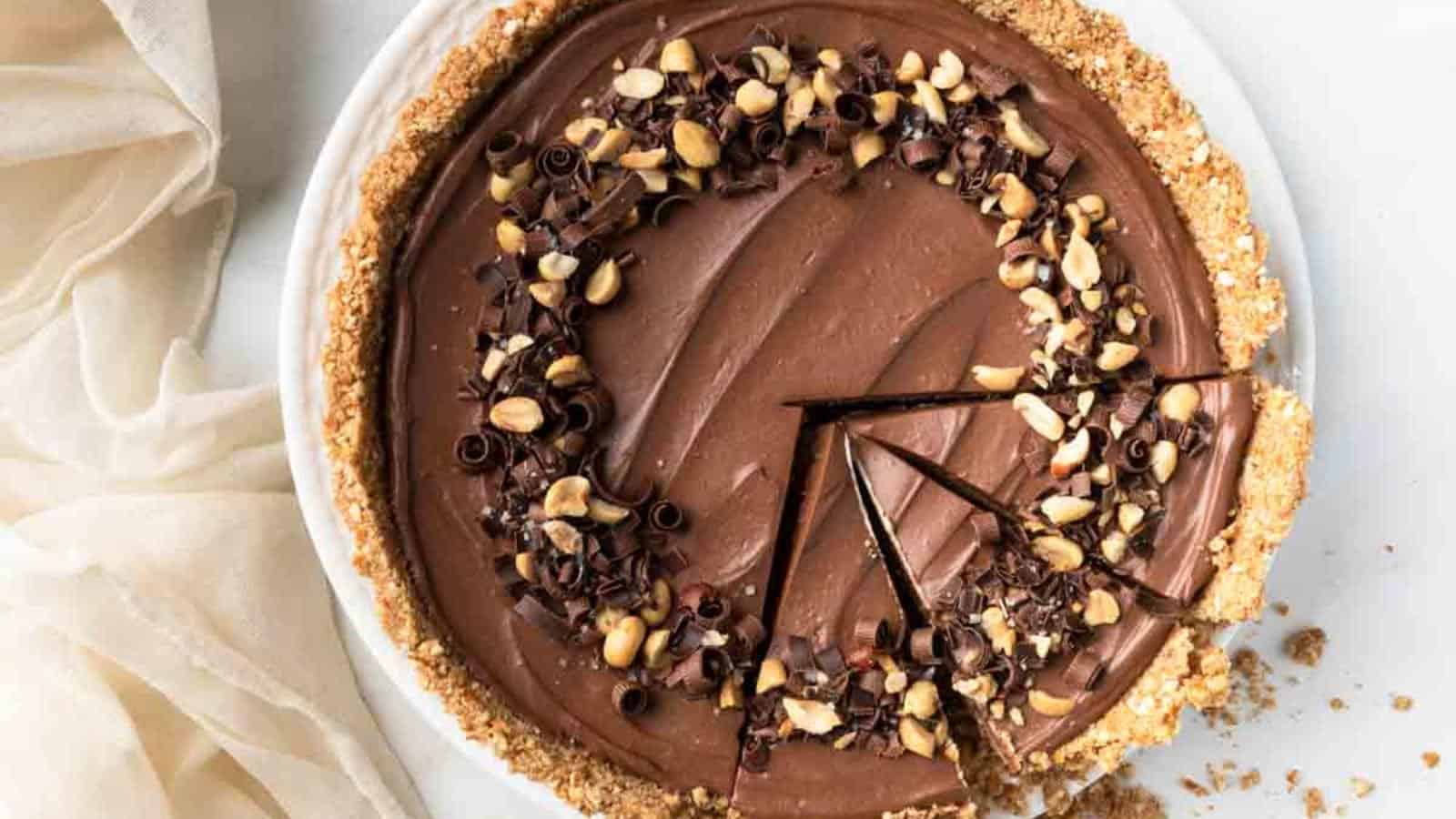 A chocolate cream pie with a crumb crust, topped with chopped peanuts and chocolate curls, with two slices cut and slightly separated from the pie.