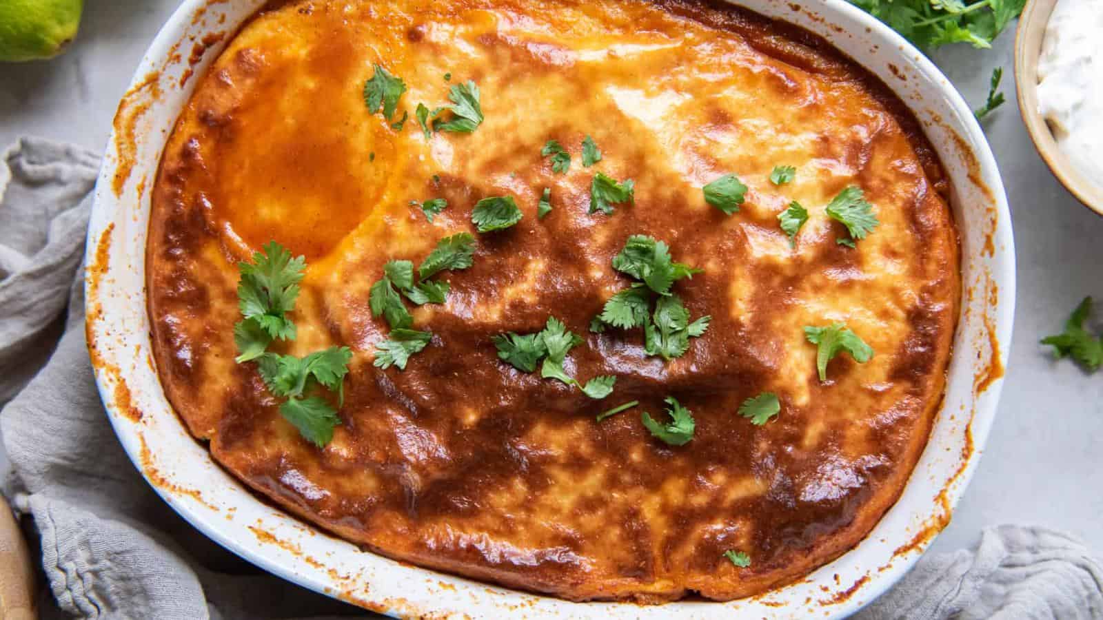 Baked enchiladas in a white oval dish, topped with red sauce and garnished with fresh cilantro leaves.