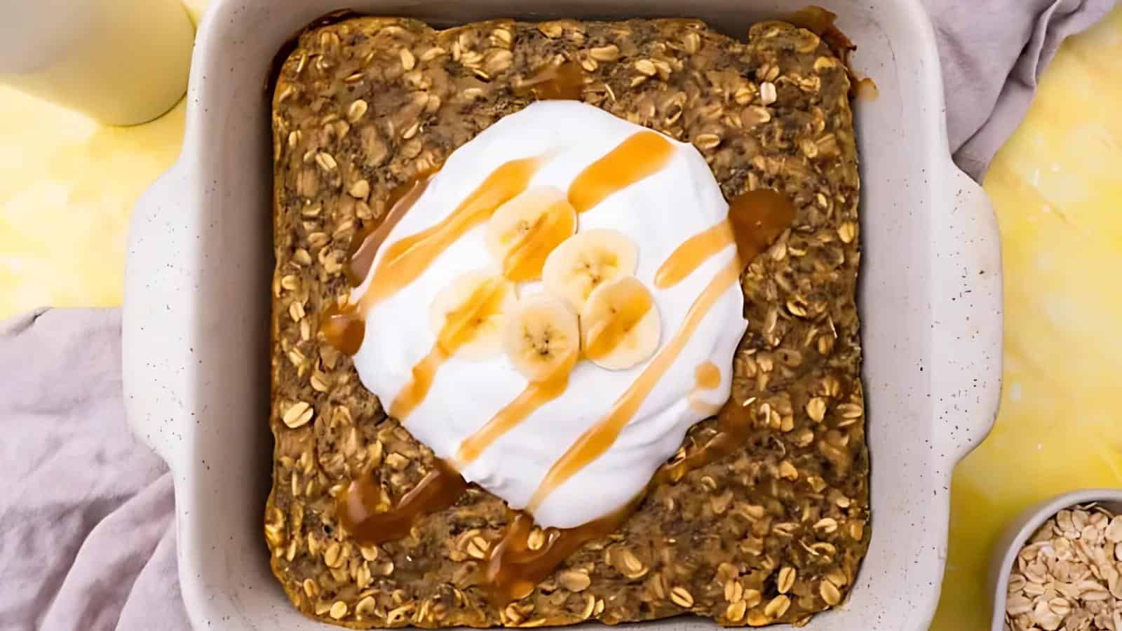 Baked oatmeal in a square dish topped with whipped cream, banana slices, and caramel drizzle.