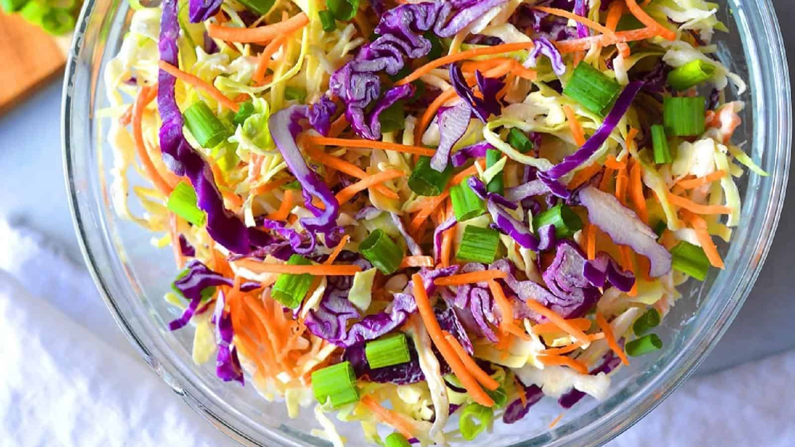 A clear bowl filled with shredded cabbage, purple cabbage, carrots, and chopped green onions.