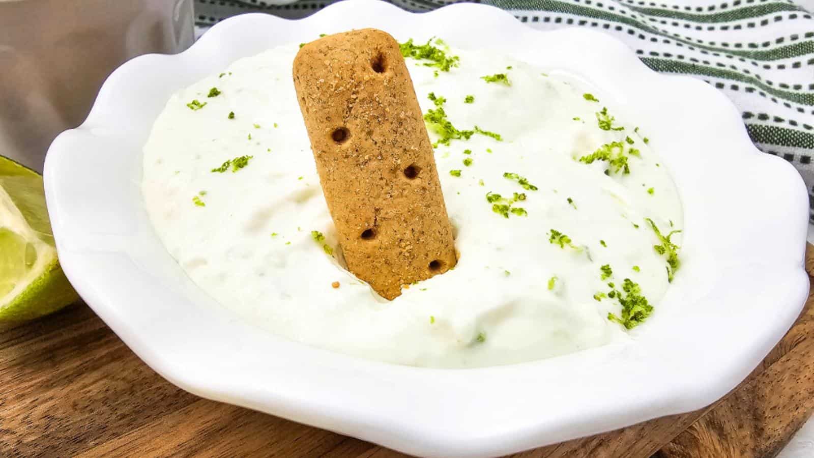 A bowl of creamy dessert topped with lime zest and a rectangular biscuit standing upright in the center.