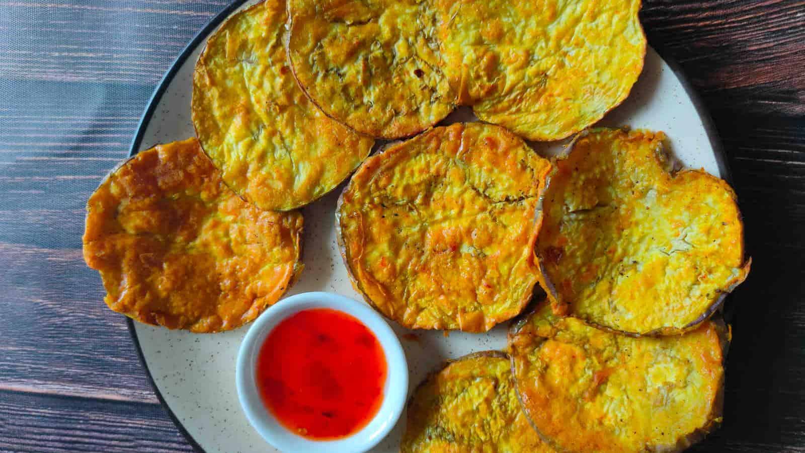 A plate of round, golden-brown fried slices with a small dish of red dipping sauce on the side.