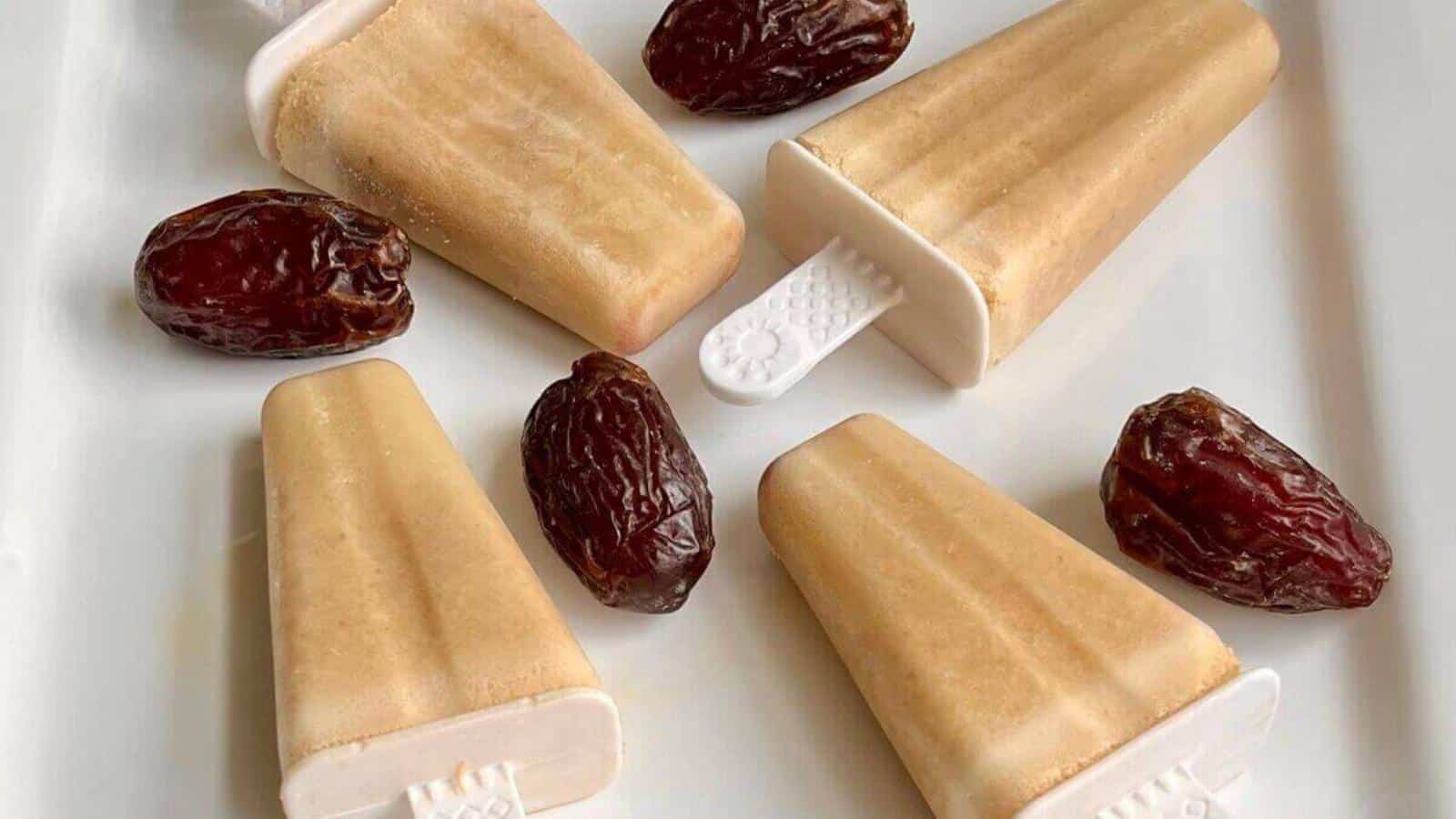 Five light brown popsicles and five whole dates arranged on a white plate.