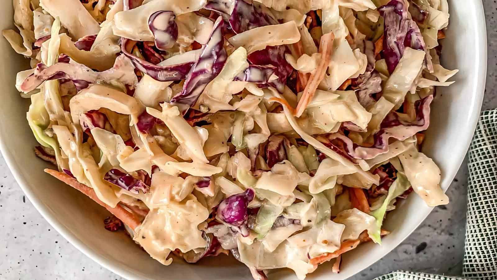 A bowl of creamy coleslaw with shredded green and purple cabbage and carrots on a light surface.