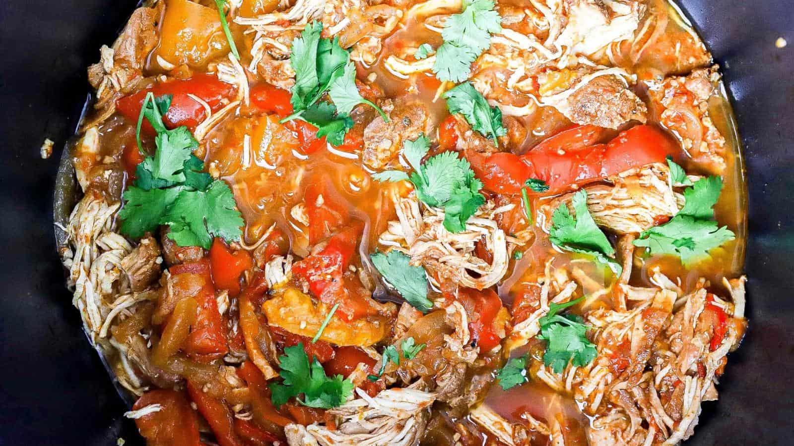 Shredded chicken, red bell peppers, tomatoes, and cilantro in a saucy mixture, viewed from above.