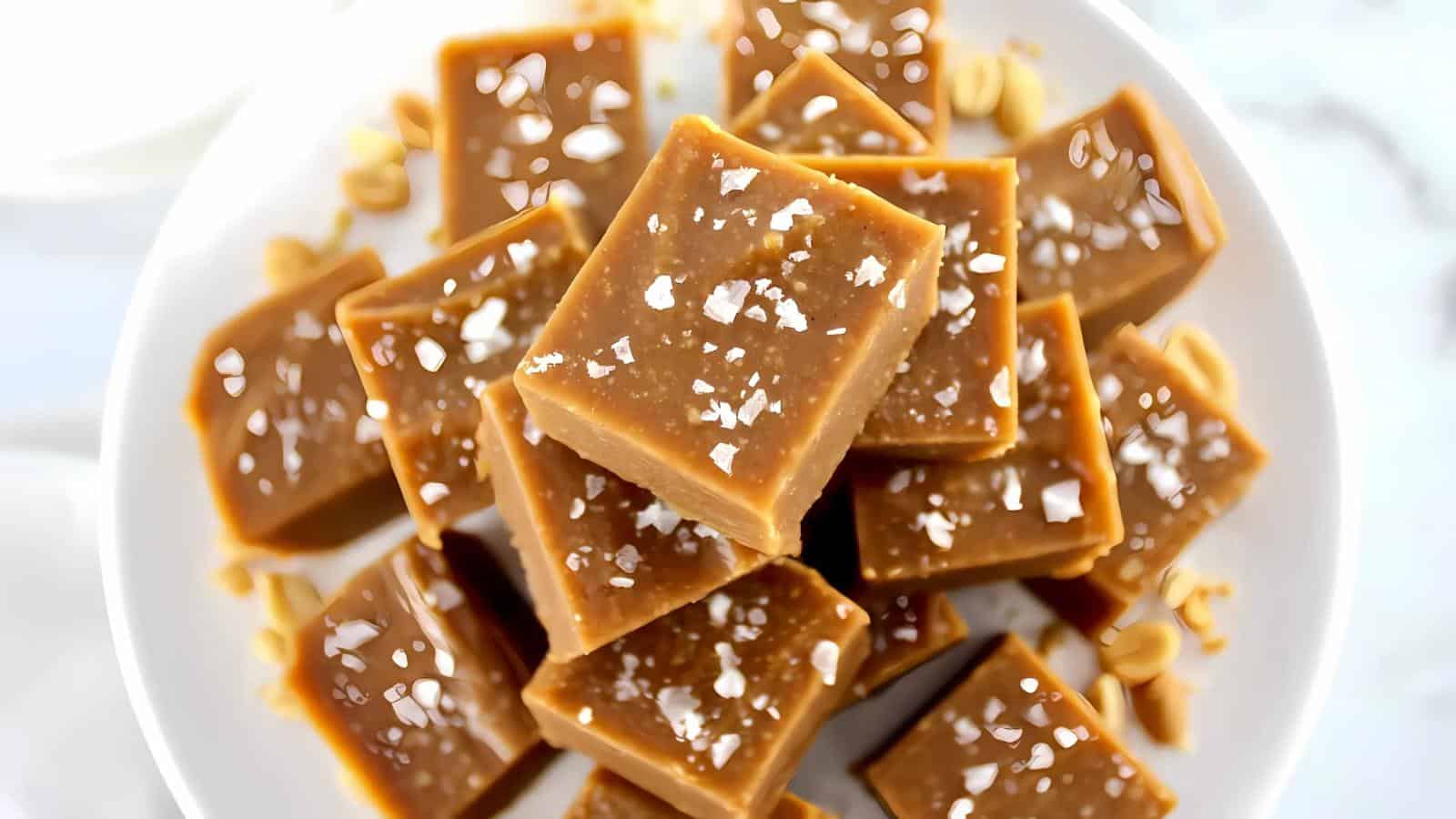A plate with several square pieces of caramel fudge topped with flaky sea salt, arranged in a pile.