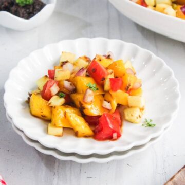 A white scalloped plate with a serving of fruit and vegetable salad containing diced peaches, tomatoes, apples, and red onions.