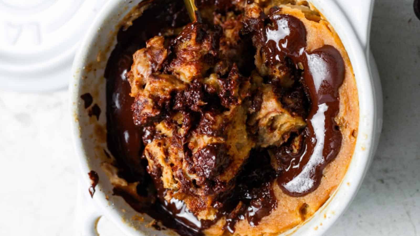 A close-up of a baked dessert in a white dish, featuring gooey melted chocolate and chunks of bread, possibly a chocolate bread pudding.