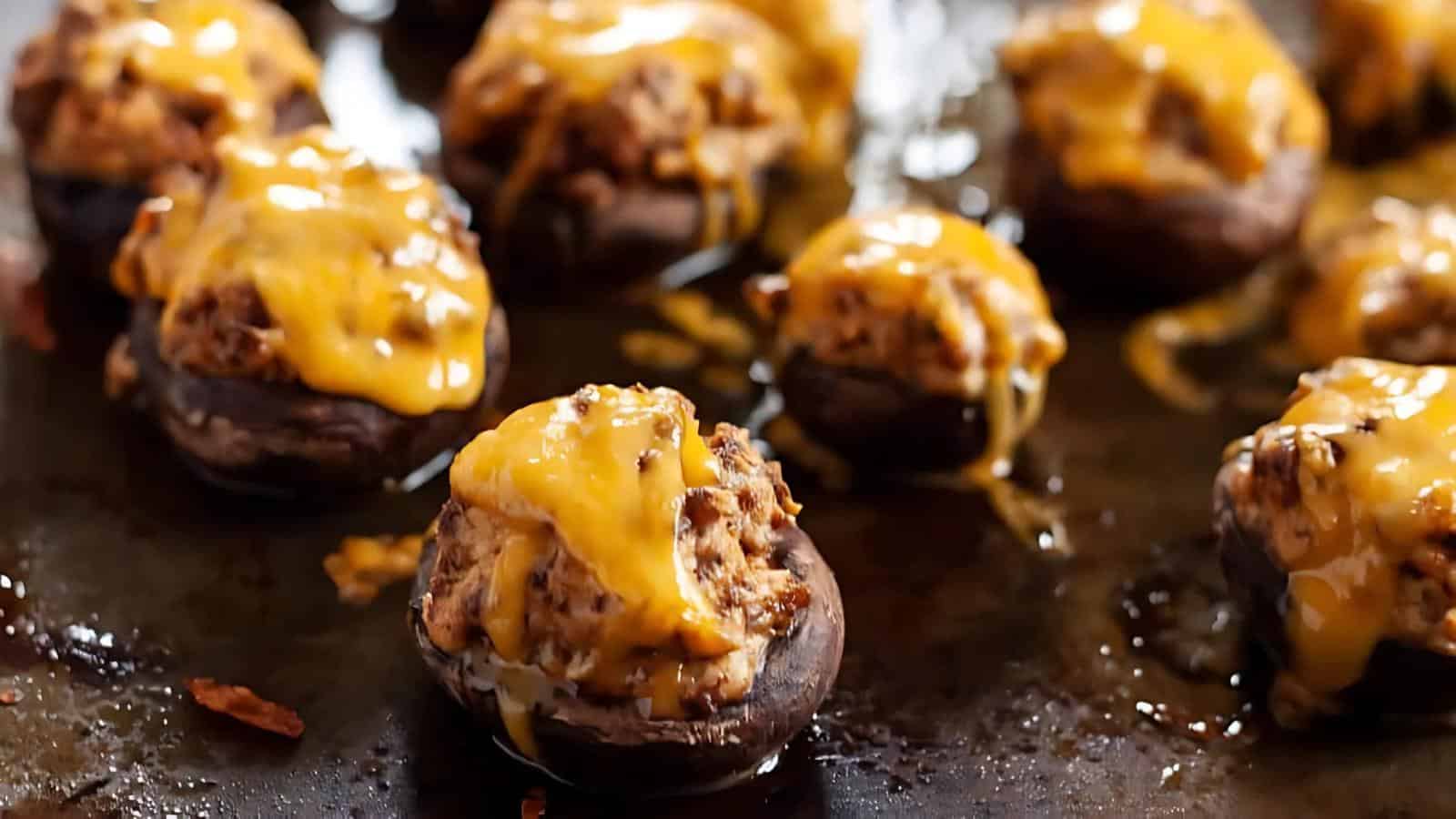 Stuffed mushrooms topped with melted cheddar cheese on a baking sheet.