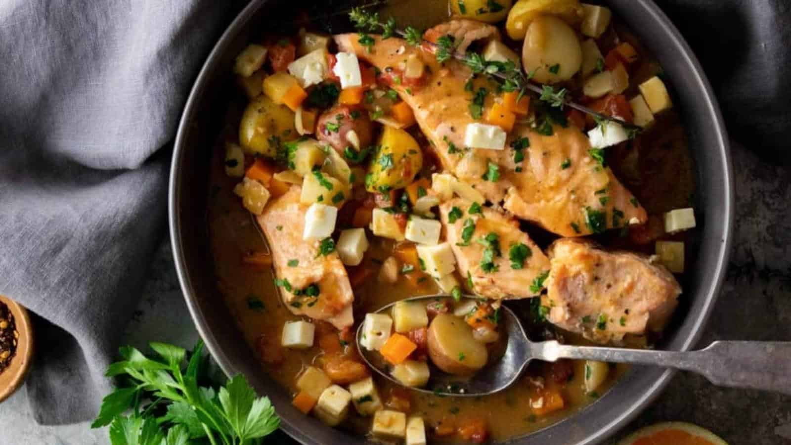 A bowl of cooked salmon with diced vegetables, potatoes, and herbs, with a spoon resting inside the bowl.