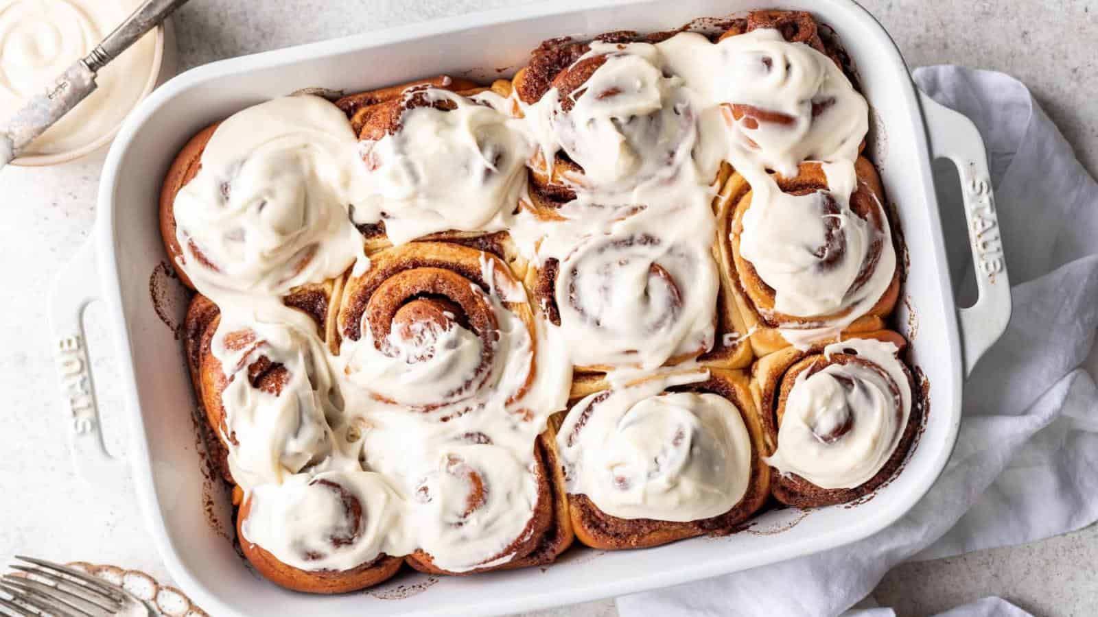 A white baking dish filled with freshly baked cinnamon rolls topped with a thick layer of white icing.