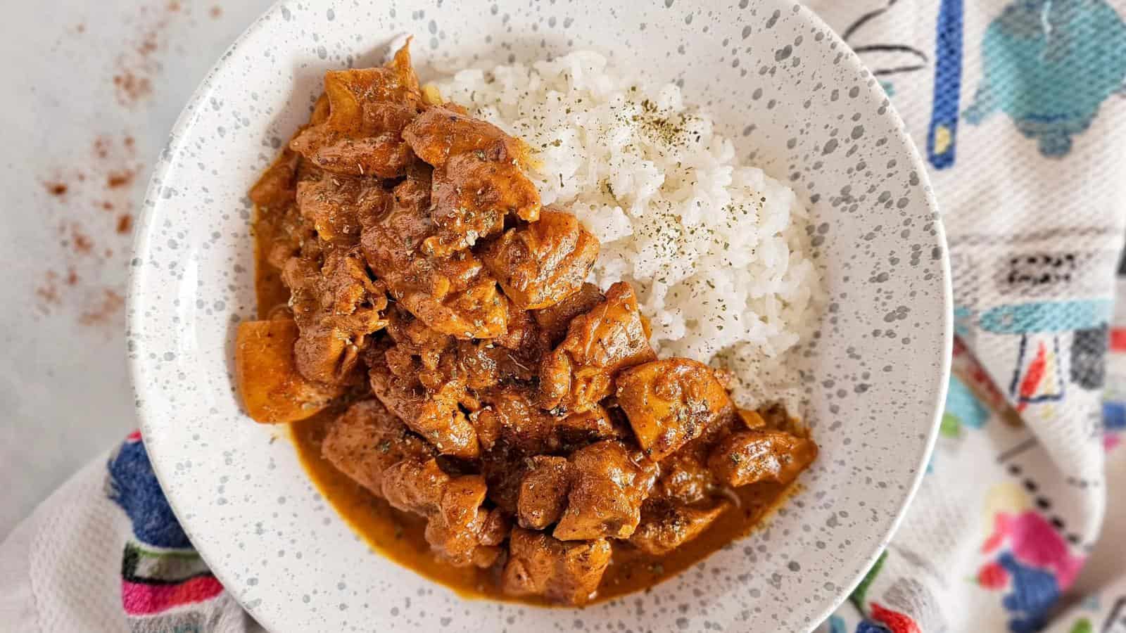 A plate of white rice served with a stew of meat and potatoes in a reddish-brown sauce, garnished with pepper.