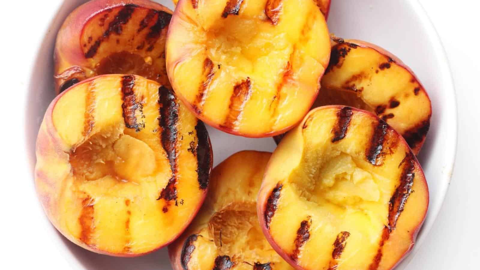 Halved peaches with grill marks are arranged in a white bowl.