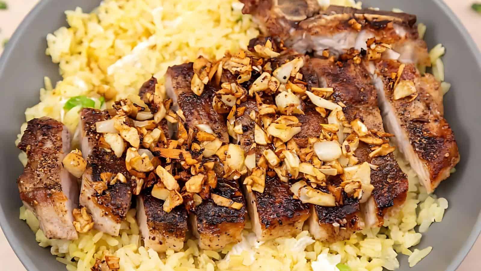 Sliced grilled meat topped with chopped garlic served over yellow rice on a plate.