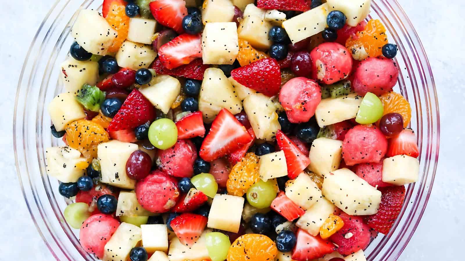 A glass bowl filled with a colorful mix of fresh fruit pieces, including strawberries, blueberries, grapes, pineapple, kiwi, mandarin oranges, and watermelon.