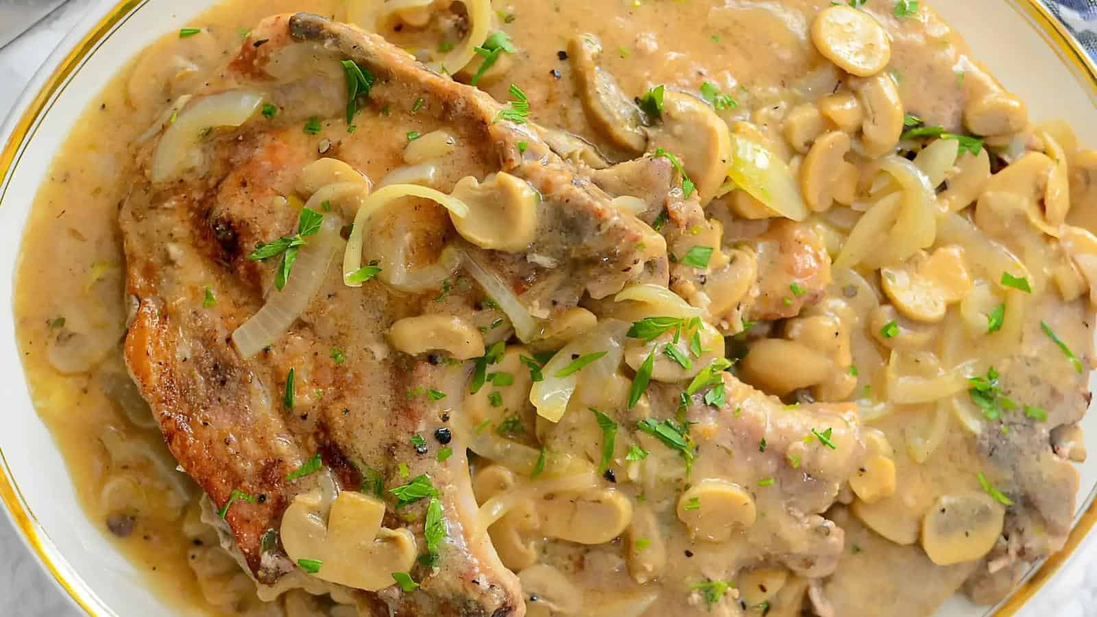 Pork chops served with sautéed onions, mushrooms, and creamy sauce, garnished with chopped parsley on a white plate.