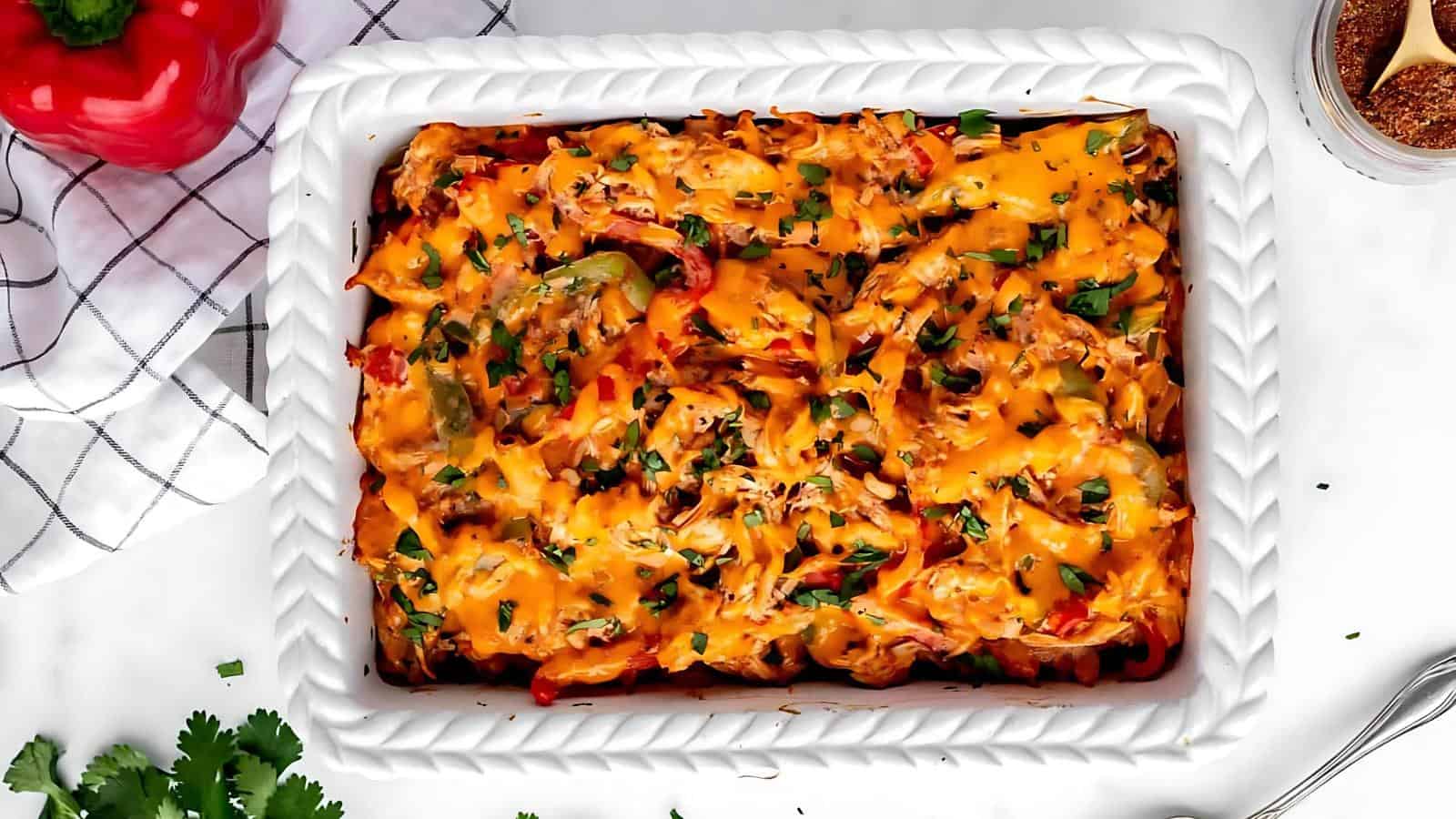 A white rectangular baking dish filled with a cheesy casserole topped with chopped herbs, photographed from above on a white surface.