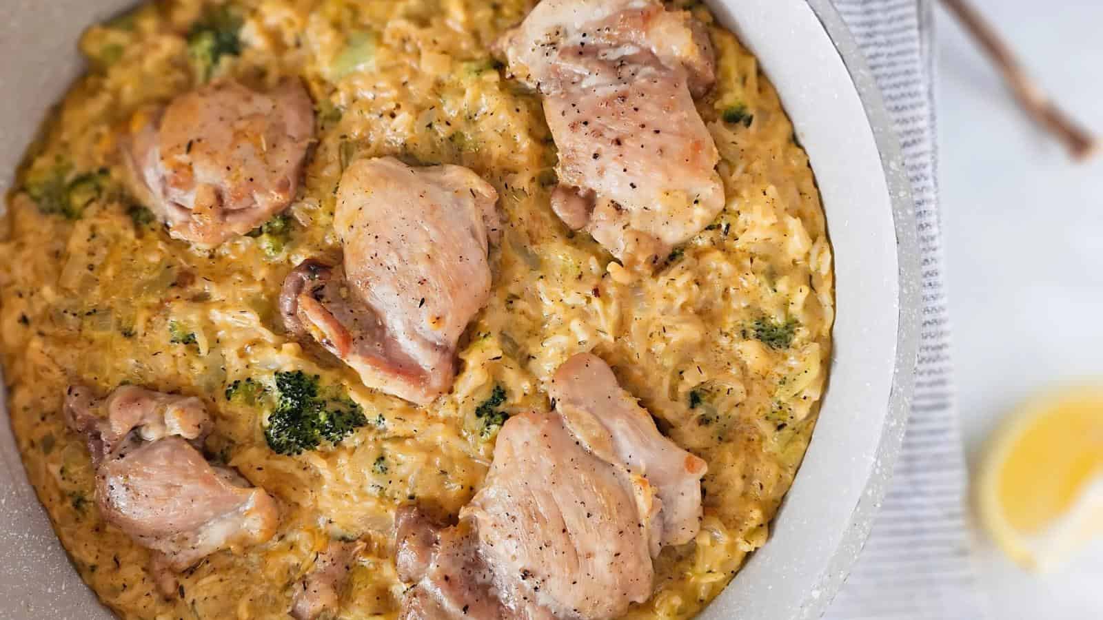 A skillet filled with creamy rice, broccoli, and five seasoned chicken thighs, photographed from above.