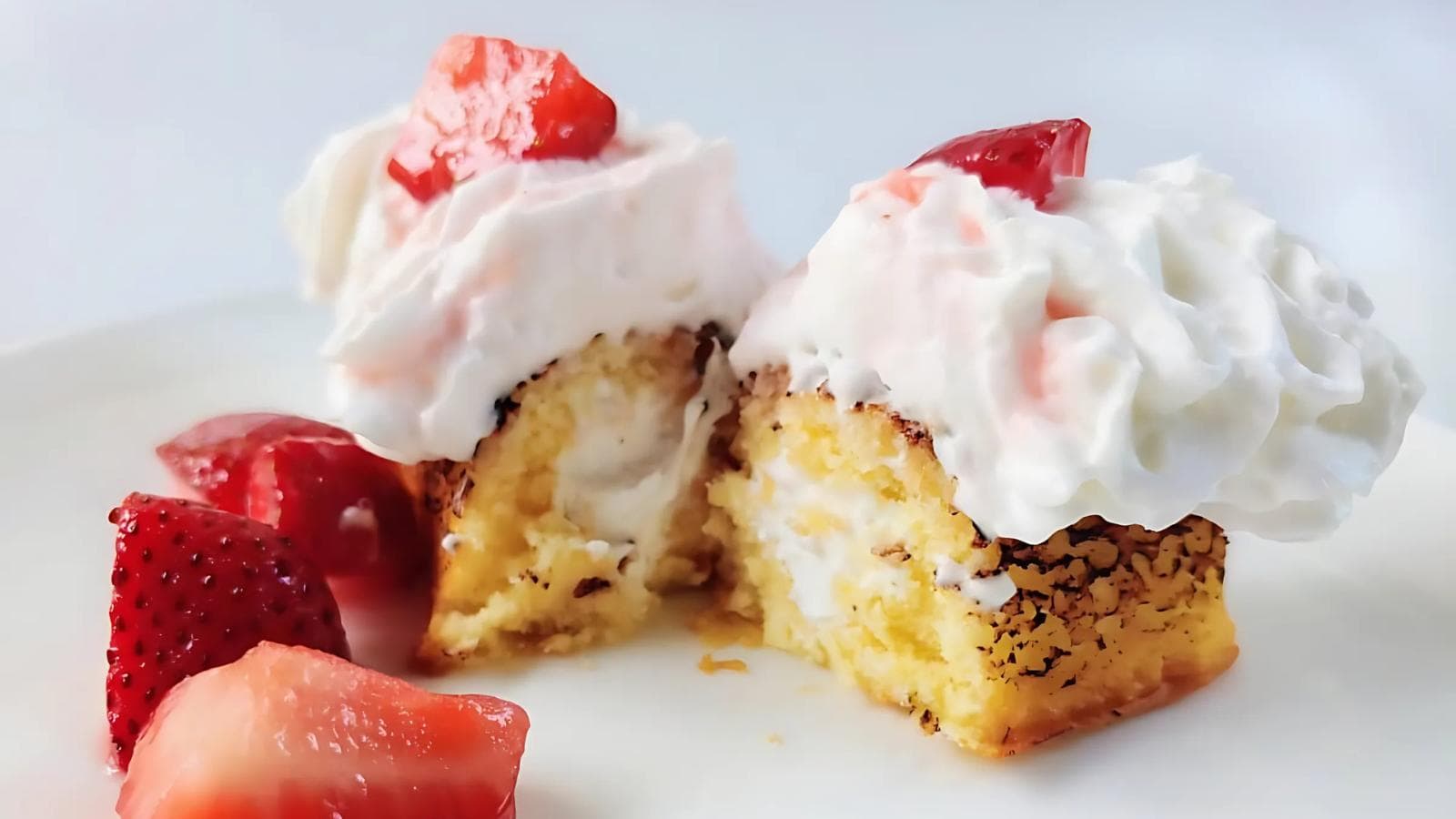 Two pieces of yellow cake with whipped cream and strawberry topping, served with extra sliced strawberries on a white plate.
