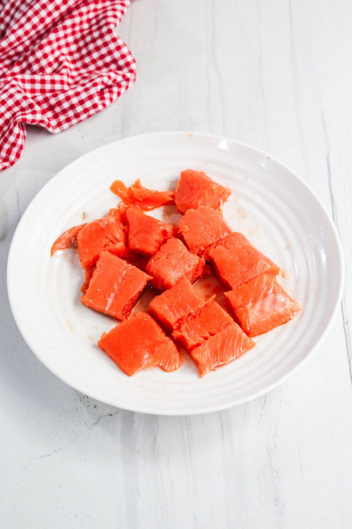 Chunks of raw salmon are arranged on a white plate with a red and white checkered cloth in the background.