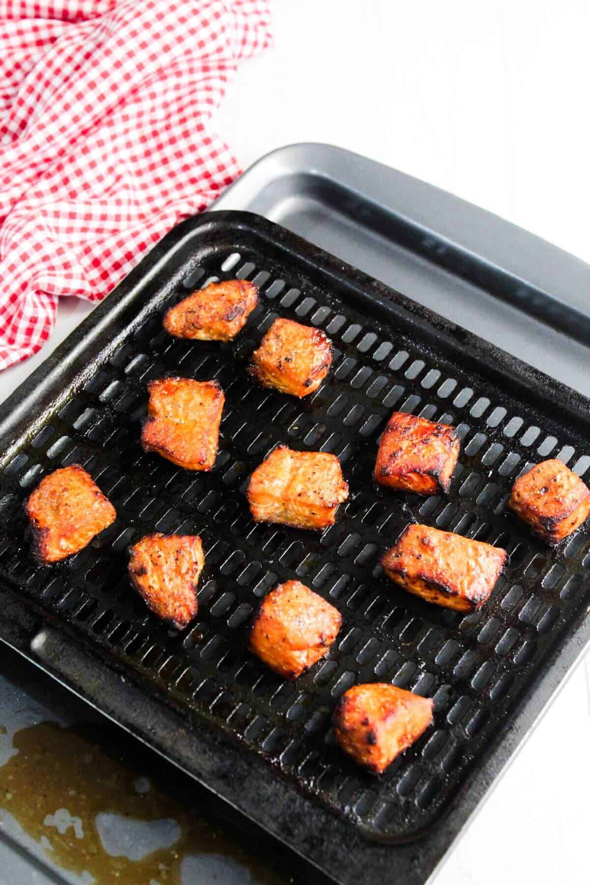 Grilled cubes of seasoned meat are arranged on a black grill tray with a red and white checkered cloth in the background.