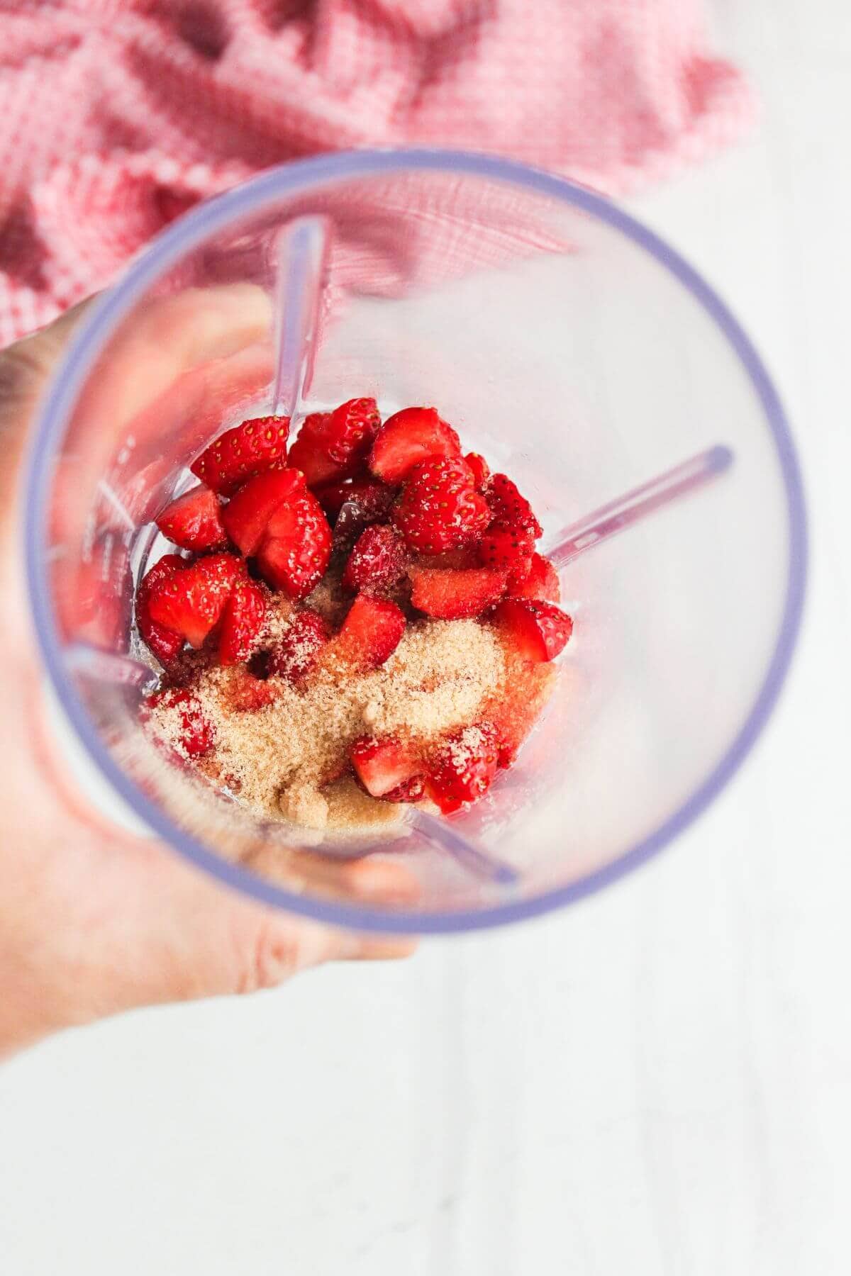 Chopped strawberries and granulated sugar inside a blender cup, ready to be blended.
