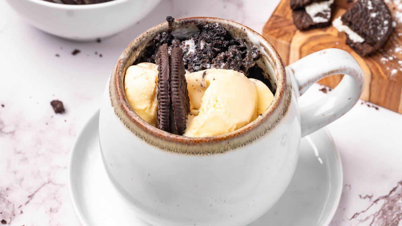 A white mug filled with vanilla ice cream, crushed chocolate sandwich cookies, and a whole cookie, placed on a saucer.