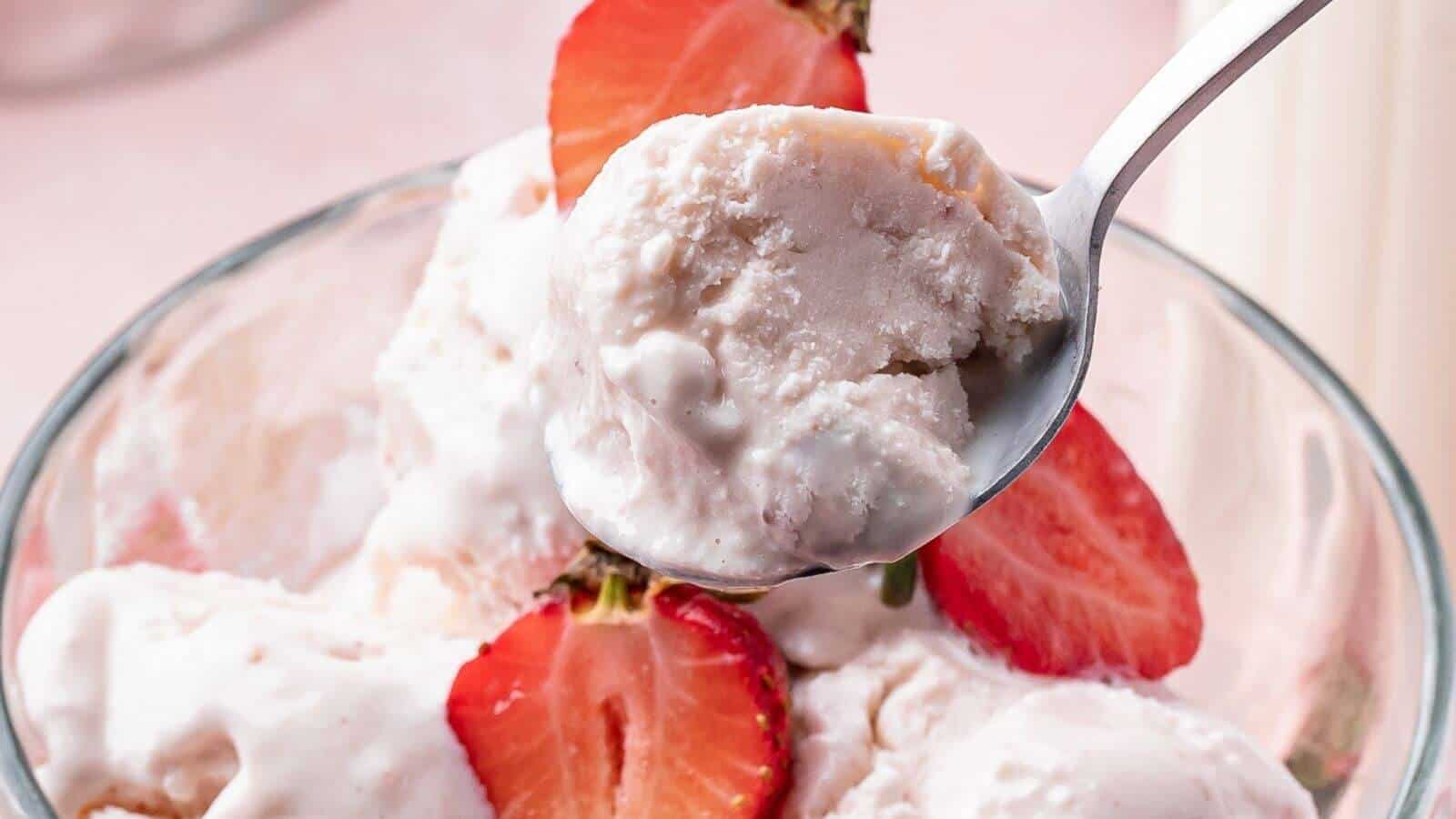 A close-up of a bowl of strawberry ice cream topped with fresh strawberry slices, with a spoon holding a scoop above the bowl.