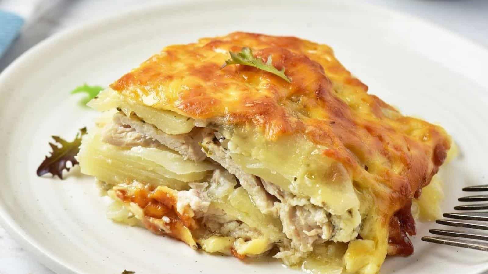 A slice of cheesy potato and meat casserole served on a white plate with a few salad leaves.