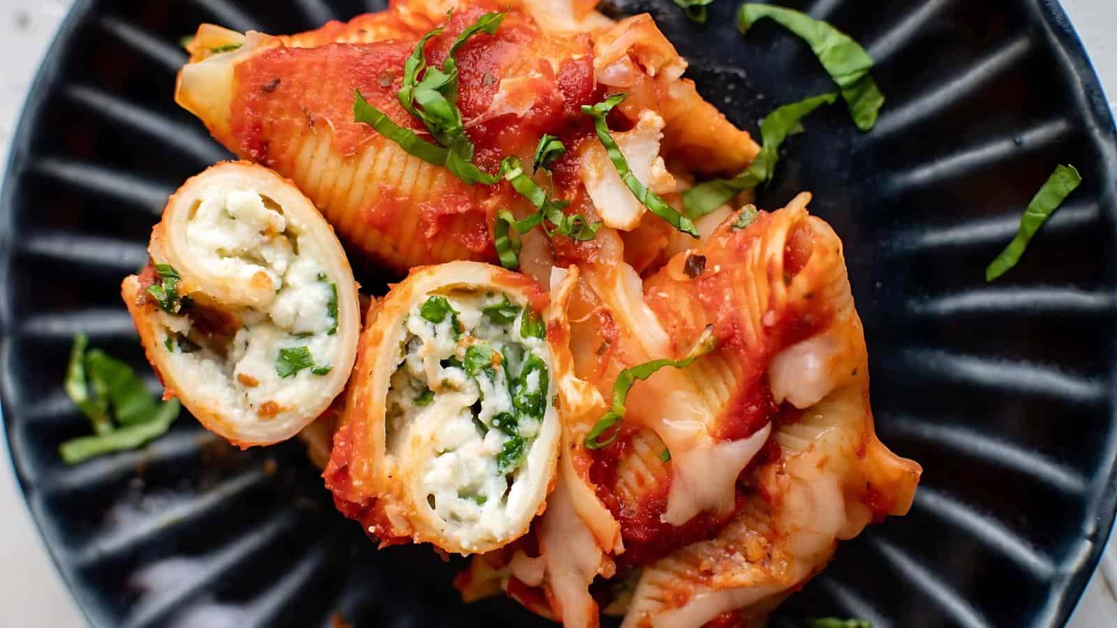 Stuffed pasta shells filled with ricotta cheese and spinach, topped with tomato sauce and garnished with fresh basil, served on a black plate.