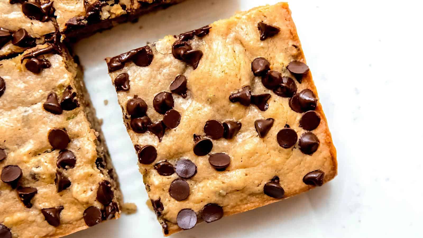 A close-up of a chocolate chip blondie bar on a white surface, with another bar partially visible beside it.