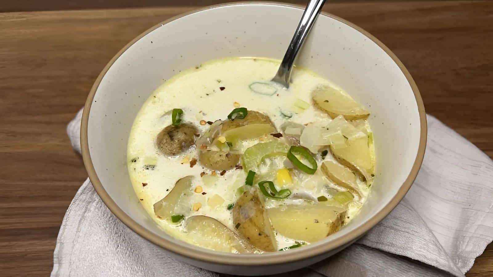 A bowl of creamy potato soup with sliced potatoes, green onions, and seasonings, served with a spoon on a white napkin.