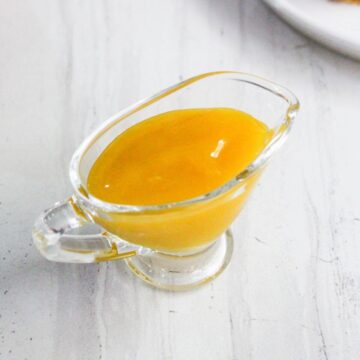 A small glass gravy boat filled with thick yellow sauce sits on a white surface.