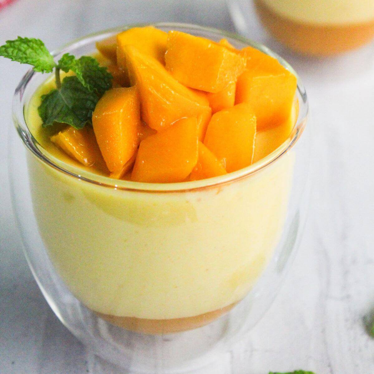 A glass cup filled with mango mousse, topped with diced mango pieces and garnished with a mint sprig.