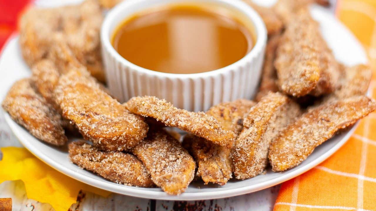 A plate of cinnamon sugar-coated fried apple slices arranged around a bowl of caramel dipping sauce.