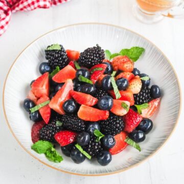 A bowl of mixed fresh berries, including strawberries, blackberries, and blueberries, garnished with mint leaves.