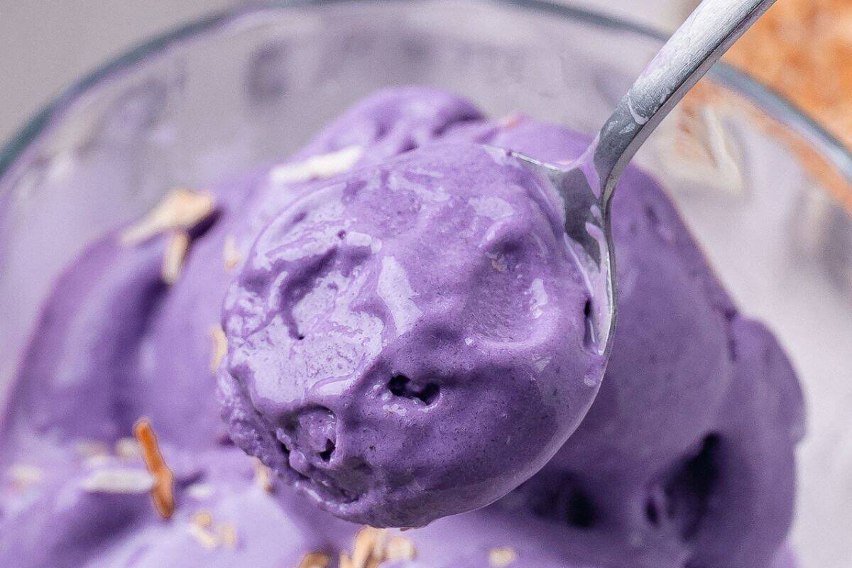 A spoonful of purple ube ice cream with slivered almonds, close-up in a glass bowl.