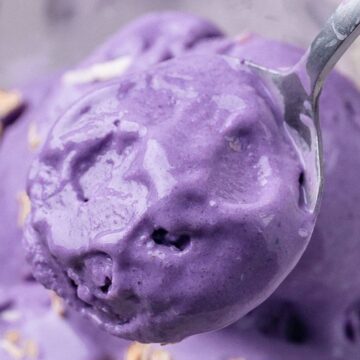 A close-up of purple ice cream in a bowl, with a spoon scooping out a portion.