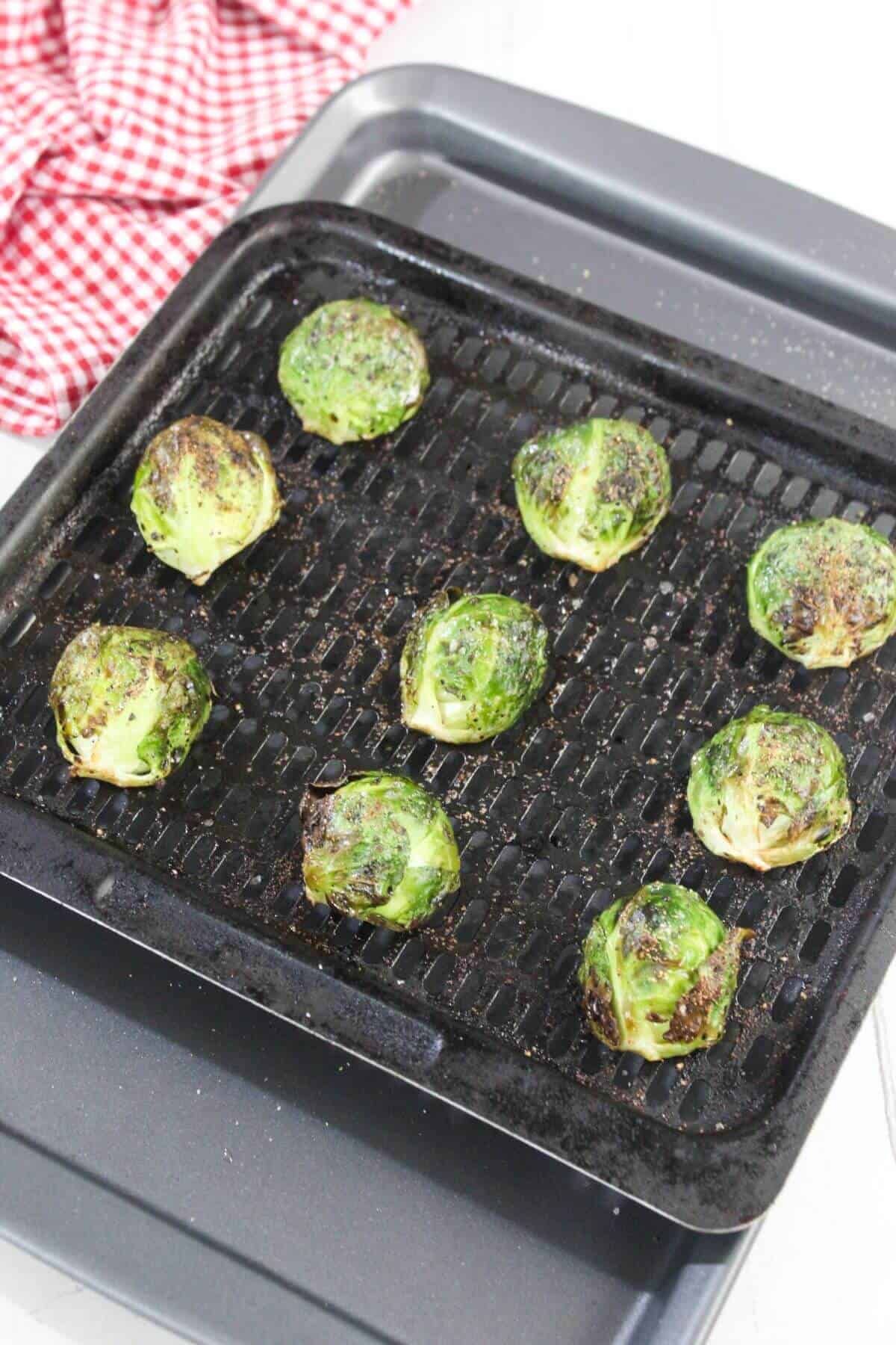 Nine roasted Brussels sprouts arranged on a black grill pan, with a red and white checkered cloth in the background.