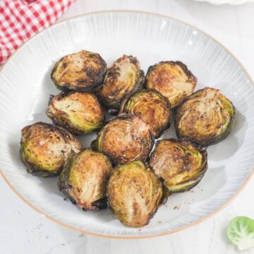 A plate of roasted Brussels sprouts halves, lightly browned and arranged in a circular pattern on a white dish.