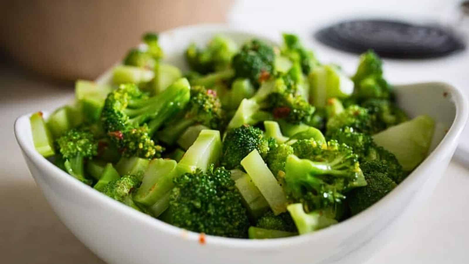A white bowl filled with steamed broccoli florets sits on a kitchen counter.